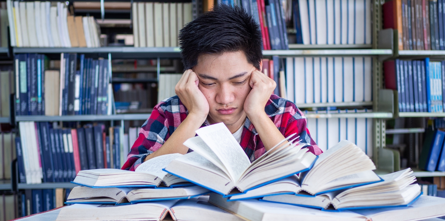 a student looking frustrated while surrounded by books